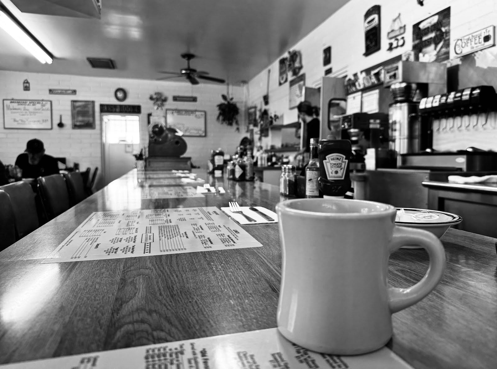 Black and white view down the diner counter, with a coffee mug and menus on the tables